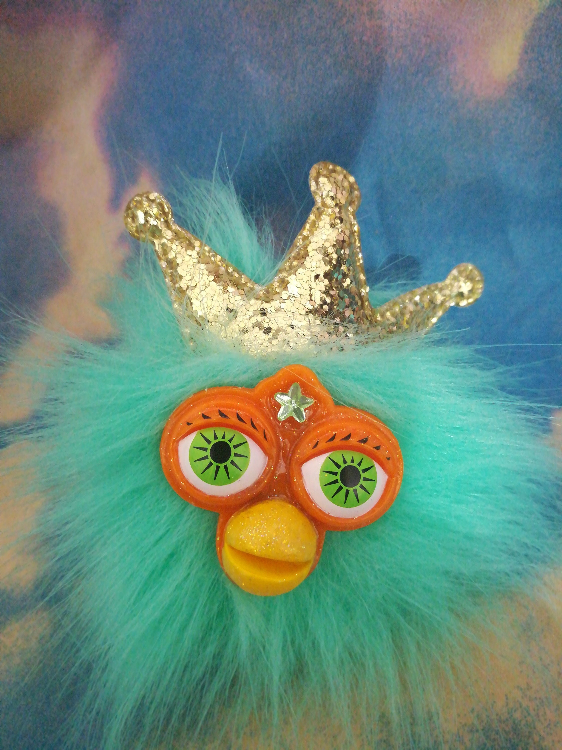 teal and orange furby keychain with a gold crown